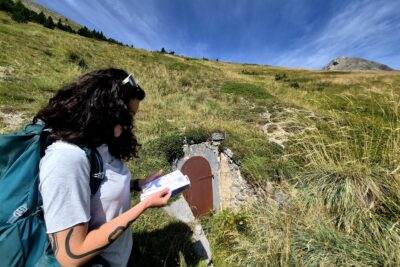 Une jeune fille dans un paysage de montagne en train de lire un livret. - Agrandir l'image 1 sur 7, fenêtre modale