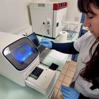 Une femme en blouse blanche devant une machine de laboratoire.