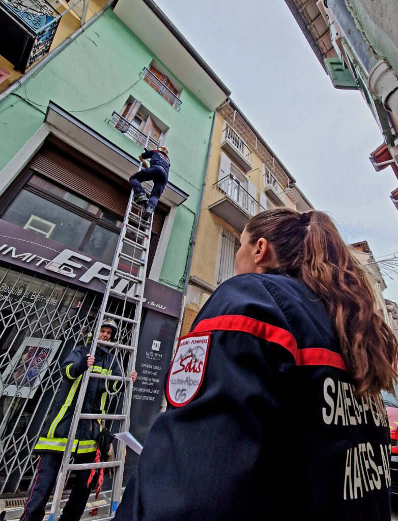 Un pompier au sommet d'une échelle entre dans un immeuble de ville par une fenêtre. - Agrandir l'image, fenêtre modale
