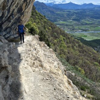 Une femme en train de randonner sur un chemin escarpé au pied d'un falaise d'escalade.