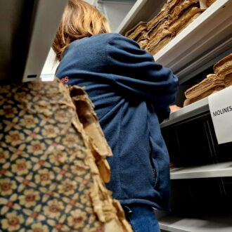 Une femme au milieu d'une allée de vieux registres au page jaunies.
