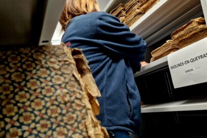 Une femme au milieu d'une allée de vieux registres au page jaunies. - Agrandir l'image, fenêtre modale