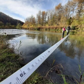 Un homme et une femme en cuissarde au milieu d'une rivière prennent des mesures dans l'eau.