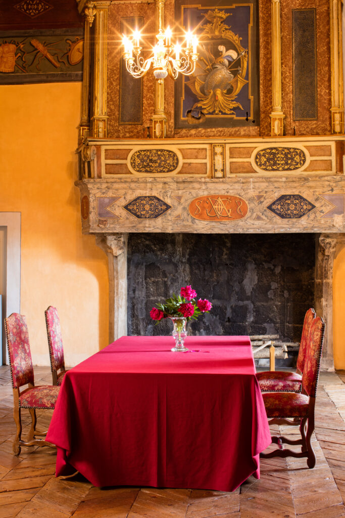Une longue table revêtue d'une nappe rouge devant la cheminée du salon d'Agoult au Château de Montmaur - Agrandir l'image, fenêtre modale