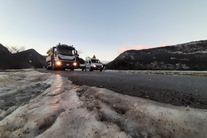 Au premier plan, une plaque de glace au bord d'une route. en deuxième plan, au milieu de la route bien noir, une saleuse du Département, feux allumée sillonne les routes afin de les sécuriser. Juste à côté, une fourgonnette du Département. Au fond des montagnes de taille raisonnable sont parsemée de neige. - Agrandir l'image, fenêtre modale