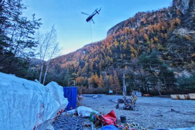Un hélicoptère dans le ciel, du matériel de chantier au premier plan et des montagnes dans le fond - Agrandir l'image 16 sur 27, fenêtre modale