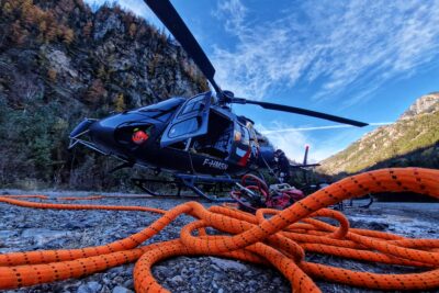 Un hélicoptère au sol et une corde orange au sol au premier plan En arrière plan des montagnes - Agrandir l'image 26 sur 27, fenêtre modale