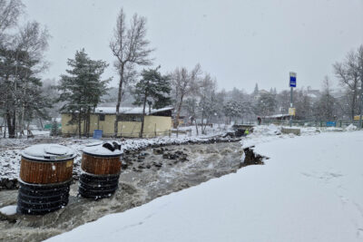 Un paysage de neige. Au centre un rovière agitée aux eaux marronasses, au milieu, charriés par les eaux deux containers à poubelle qui tentent de résiter à la force de l'eau - Agrandir l'image 1 sur 4, fenêtre modale