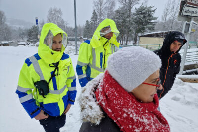 Dans un paysage de neige, la photo est centrée sur quatre personne emmitouflée et portant des capuche pour se protéger des flocons. Il s'agit des trois hommes, dont deux habillés de blousons jaune fluo et bleu électrique. Le troisième d'un blouson de sport noir. La femme au premier plan porte un bonnet et une grosse écharpe rouge. - Agrandir l'image 3 sur 4, fenêtre modale