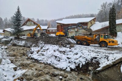 Photo paysage avec au premier plan le torrent Risoul, aux eaux marron en furie. En second plan des engins de chantier jaune, des pelles mécaniques et un camion benne, travaillent à enlever les 30 000 m3 de sédiments. En arrière plan on distingue la mairie de Risoul. Il neige. Une pellicule blanche est en train de se former. - Agrandir l'image 5 sur 12, fenêtre modale