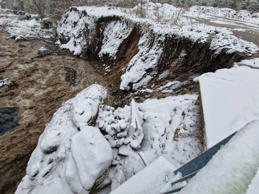 Un torrent au eau marron en furie, une culée de pont effondrée, une berge complètement érodée. Le tout sous une pellicule de neige. - Agrandir l'image, fenêtre modale