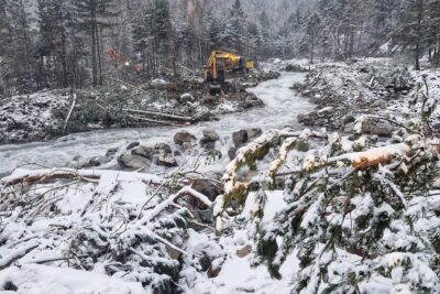 Au milieu d'un paysage neigeux et brumeux, un torrent sinueux. Sur la berge gauche des pelles mécaniques s'activent. Sur la berge droite, des branchages et troncs arrachés par la crue. - Agrandir l'image 12 sur 12, fenêtre modale