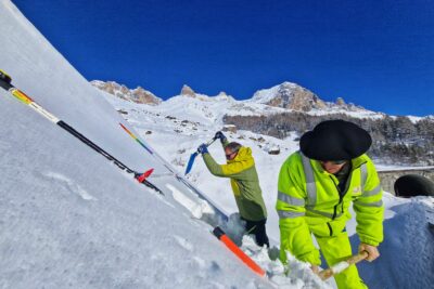 Dans un paysage blanc, deux hommes creusent à la pelle dans une pente couverte de neige. En arrière plan on distingue un tunnel et des voitures agrées en épis. - Agrandir l'image 3 sur 13, fenêtre modale