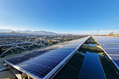 Un champ de panneaux photovoltaïques flottant au premier plan et au loin une ligne d'horizon montagneuse. Le ciel est bleu légèrement voilé de nuage. - Agrandir l'image 4 sur 4, fenêtre modale