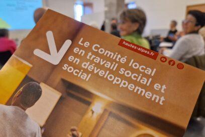 Au premier plan un prospectus intitulé "Le comité local en travail social et en développement social". En fond, en flou, une assistance de personnes assise sur des chaise en nombre important. - Agrandir l'image, fenêtre modale