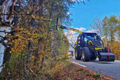 La photo est plus ou moins coupé en deux moitié égale. Sur la partie droite, une imposant tracteur noir et vert pomme est muni d'un bras mécanique articulé muni de disques aux dents tranchantes. Disque en train de couper les branches d'arbres situé sur le bas côté d'un route qui vienne géner la visibilité. En arrière plan, on distingue une camionnette blanche et deux hommes en tout petit vête de vêtement de travail bleu électrique et jaune fluo. Le ciel est bleu parsemé de quelques nuage. - Agrandir l'image 2 sur 7, fenêtre modale