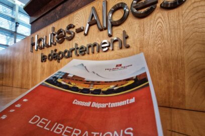 Sur un pan de bois des lettres métalliques "Hautes-Alpes, le Département". Juste en dessous un document qui semble plonger vers les lettres. Dessus ont peu lire "Conseil Départemental, délibération". - Agrandir l'image, fenêtre modale