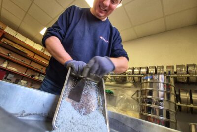 Un agent laboratoire routier départemental est en train de transféré du sel routier d'un bas métallique à un atre plus gros à l'aide d'une spatule - Agrandir l'image 6 sur 8, fenêtre modale