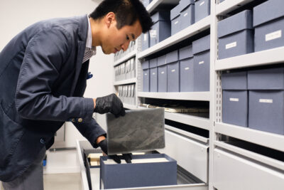 Un agent, muni de gants, range précautionneusement des documents dans des boites de stockage - Agrandir l'image 7 sur 9, fenêtre modale
