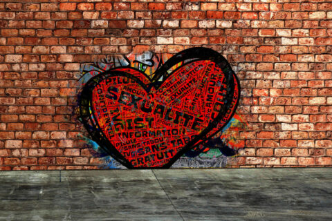 Un mur de brique rouges sur lequel a été tagué un cœur rempli de mots clefs liés à la sexualité