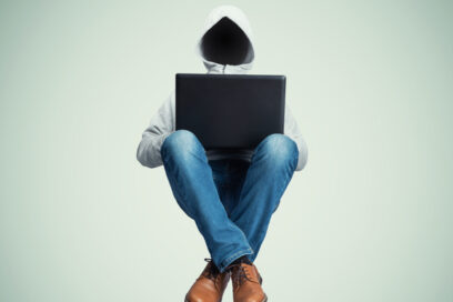 Au milieux de l'image un personnage vêtu d'un jean, de chaussures de ville marron et d'un sweat à capuche blanc gris est en lévitation dans une position en tailleur. Entre ses genoux un ordinateur portable noir. En lieu et place de son visage, du vide. Le fond de l'image est uni, couleur neutre tirant un peu sur le vert. - Agrandir l'image, fenêtre modale