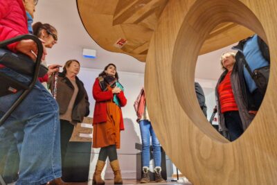 Un groupe de personnes malvoyante autour de la guide du musée en train de commenter leur visite. Au premier plan, une oeuvre en blois qui ressemble à une table, dont le pied forme un o géant. - Agrandir l'image 12 sur 13, fenêtre modale