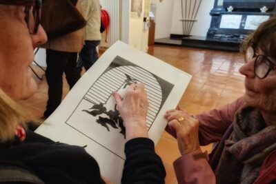 Au premier plan une dame mal voyante parcours du doigt la reproduction sur une feuille thermo gonflée de "La désolation des Océanides au pied du roc où Prométhée est enchainé". Une autre dame accroupie lui tient la feuille. - Agrandir l'image 10 sur 13, fenêtre modale