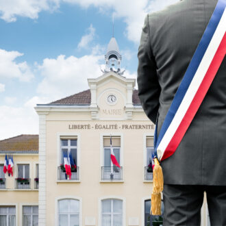 Silhouette de maire portant l'écharpe tricolore devant sa mairie