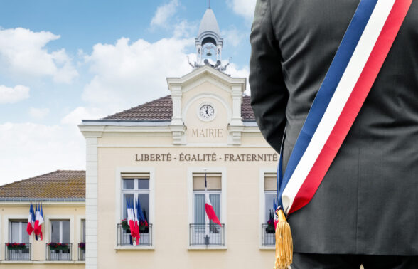 Silhouette de maire portant l'écharpe tricolore devant sa mairie