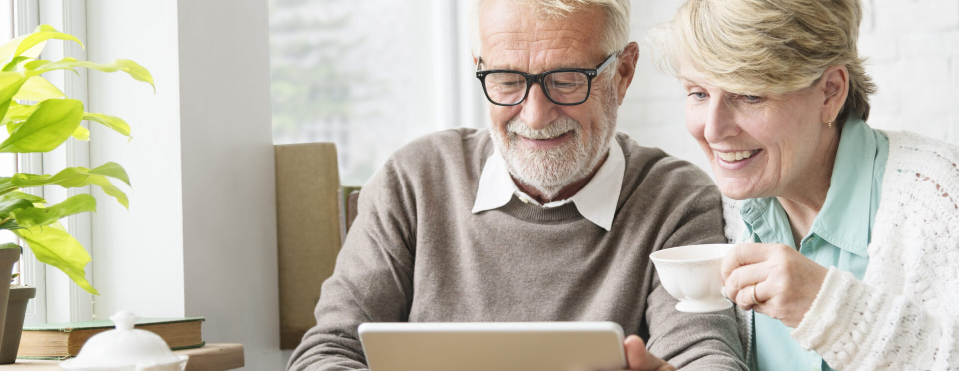 Couple de personnages âgées utilisant une tablette numérique en buvant le thé