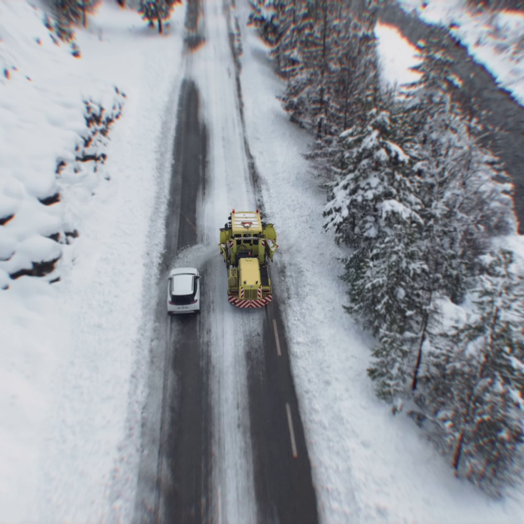 Une voiture double un chasse-neige en intervention sur une route enneigée