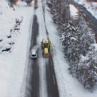 Une voiture double un chasse-neige en intervention sur une route enneigée