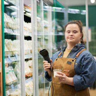 Femme en situation de handicap travaillant dans un supermarché. Elle scanne un produit frais en tenue d'employée.