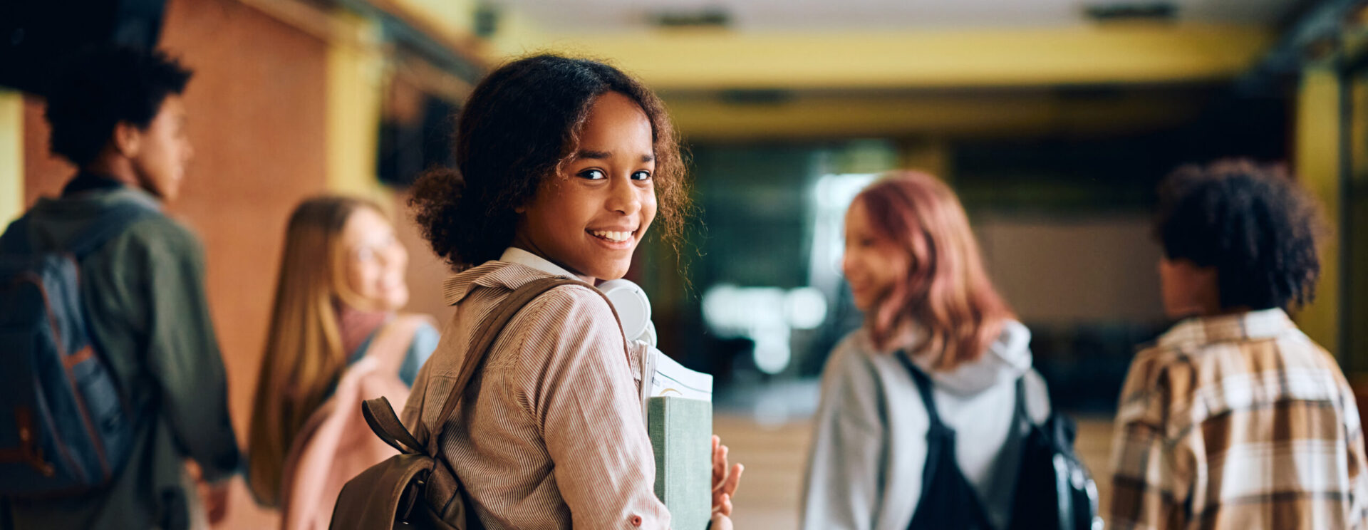Une collégienne souriante portant un cartable et des dossiers dans les bras.