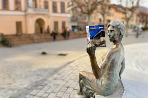 Montage photo de la statue "La liseuse" à Gap lisant un exemplaire du Magazine départemental