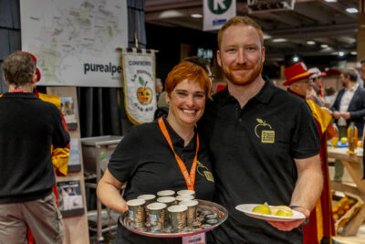 Deux exposants qui sourient au photographe avec des plateaux remplis de produits haut-alpins - Agrandir l'image 7 sur 19, fenêtre modale